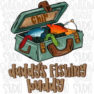 May include: A green tackle box with the word "Chip" written on the lid. The box is open and contains fishing lures, including a red and orange lure, a blue lure, and a green worm. The text "daddy's fishing buddy" is written below the tackle box.