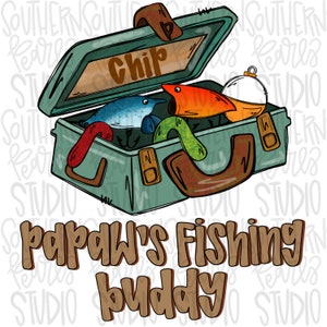 May include: A green tackle box with the word "Chip" written on the lid. The box is open and contains fishing lures, including a blue and white lure, an orange and red lure, and a green worm lure. The text "Papaw's Fishing Buddy" is written below the tackle box.