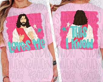May include: A light pink t-shirt featuring a graphic of a figure with long brown hair and a red sash. The front displays the text "Loves Me" in teal, while the back shows the same figure from behind with the text "This I Know" in teal.