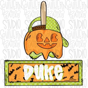 May include: A green and orange Halloween-themed caramel apple with a jack-o'-lantern face and a green and white checkered hat. The apple is on a green and orange sign with the word "Duke" in white letters.