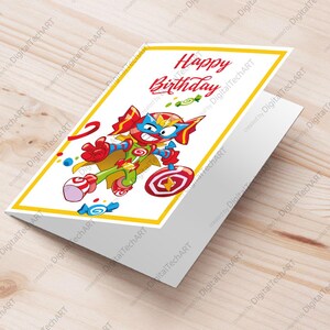 Może przedstawiać: Złożona kartka urodzinowa z ilustracją superbohatera z kreskówek. Karta zawiera napis "Happy Birthday" w czerwonym skrypcie. Superbohater jest w dynamicznej pozie, otoczony kolorowymi cukierkami i lizakiem.