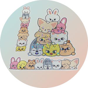 May include: A circular sticker with cartoon animal characters in various colours. The sticker features stacked animals, including bunnies, foxes, and dogs, with glitter accents. The design has a gradient background of light blue and pink.