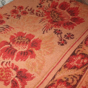 May include: A vintage woven throw blanket with a floral pattern in shades of red, orange, and brown. The blanket has a textured surface and a fringe border.