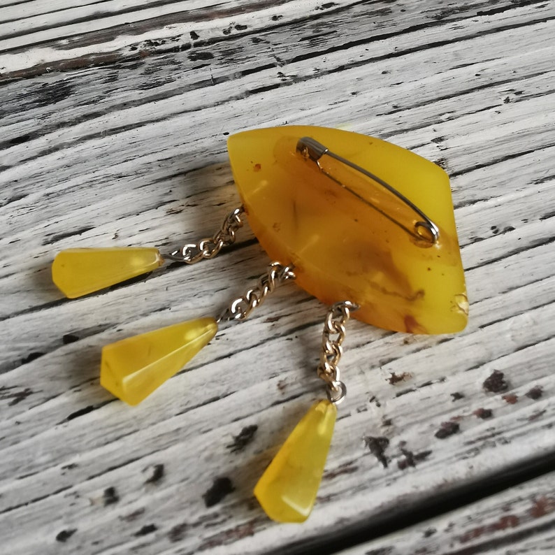 Op de afbeelding: Een gele barnsteen broche met een traanvorm en drie hangende traanvormige bedels bevestigd aan een gouden ketting.