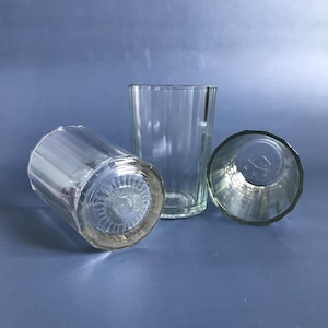 Puede incluir: Tres vasos de vidrio transparente para beber con un diseño acanalado. Los vasos están sobre una superficie azul.