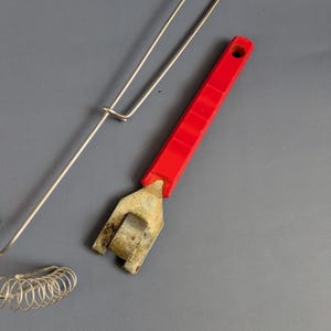 May include: A red-handled can opener with a silver metal head and a silver wire whisk. The can opener has a rectangular handle with a hole at the end. The whisk has a coiled wire design.