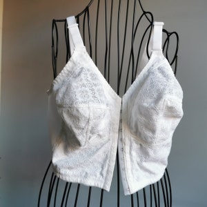 Può includere: Reggiseno in pizzo bianco con chiusura frontale. Il reggiseno presenta un delicato motivo floreale ed è realizzato in un materiale morbido ed elastico.