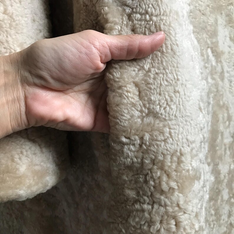 Op de afbeelding: Close-up van de zachte, beige fleecevoering van een jas. De fleece is getextureerd en heeft een subtiel patroon.