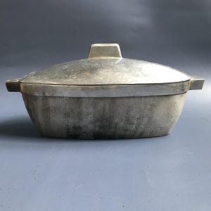 May include: A vintage aluminum oval baking dish with a lid. The dish has a slightly textured surface and is showing signs of age and use.