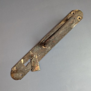 Könnte beinhalten: Ein antiker, verwitterter Metalltürgriff mit einer langen, rechteckigen Rückplatte. Der Griff hat eine dunkel, rostbraune Farbe mit einem Schlüsselloch und einem kleinen, angebrachten Riegel. Der Griff ist etwa 20 cm lang.
