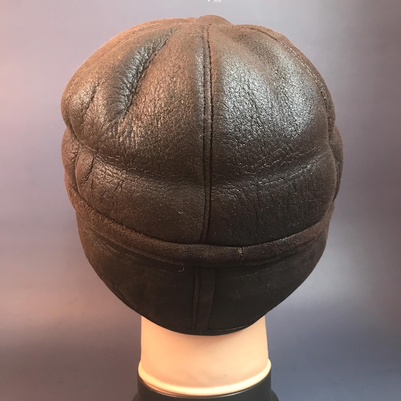 May include: A dark brown leather hat with a rounded crown and a brim. The hat appears to be made of a soft, textured leather. The hat is designed to cover the head and ears.