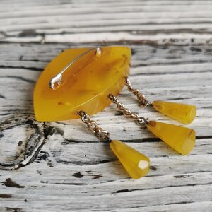 Op de afbeelding: Een gele barnsteen broche met een traanvorm en een ketting met drie hangende traanvormige barnsteenstukken.