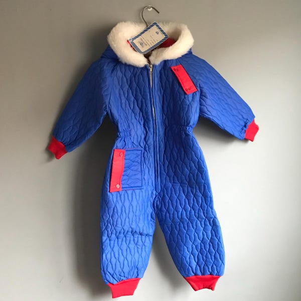 May include: Blue quilted snowsuit with a red zip and red trim. The snowsuit has a white faux fur hood and a tag that reads "Snowsuit Size 12 Months".