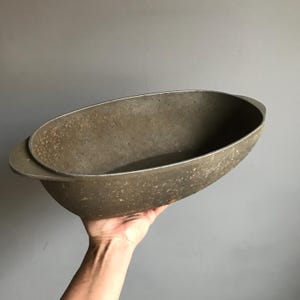 May include: A vintage oval-shaped aluminum baking dish with two handles. The dish has a speckled, worn surface.