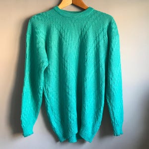 May include: A teal blue knitted jumper with a cable knit pattern.