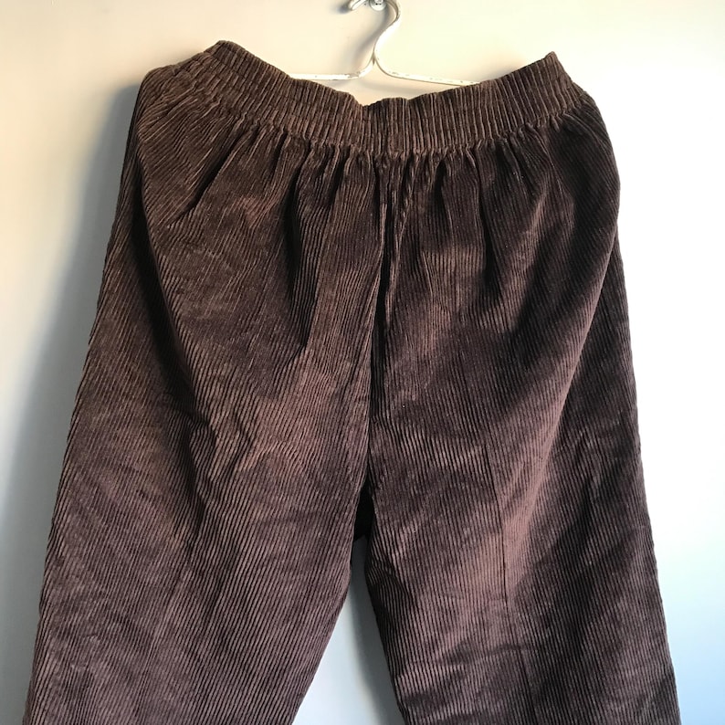 May include: Brown corduroy pants with a wide waistband and a relaxed fit.