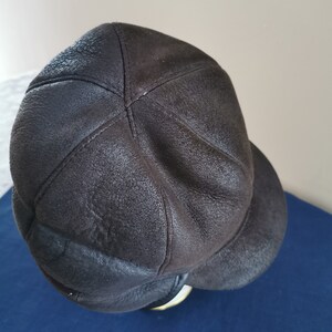 May include: A dark brown leather cap with a rounded crown and a short, curved brim. The cap has a textured surface and visible stitching, suggesting a vintage or handcrafted style. The brim is a darker shade of brown.