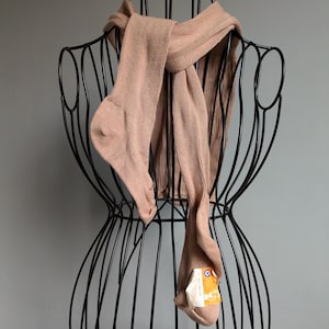 May include: Light brown tights draped over a black wire mannequin. The tights are folded over the mannequin's shoulders and torso. A tag is attached to one foot of the tights.