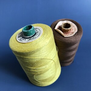 May include: Two spools of thread, one yellow and one brown. The yellow spool has a label that reads "44/1 250m".