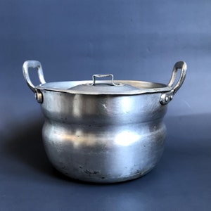 May include: A silver aluminum pot with a lid and two handles. The pot has a rounded bottom and a slightly flared top.