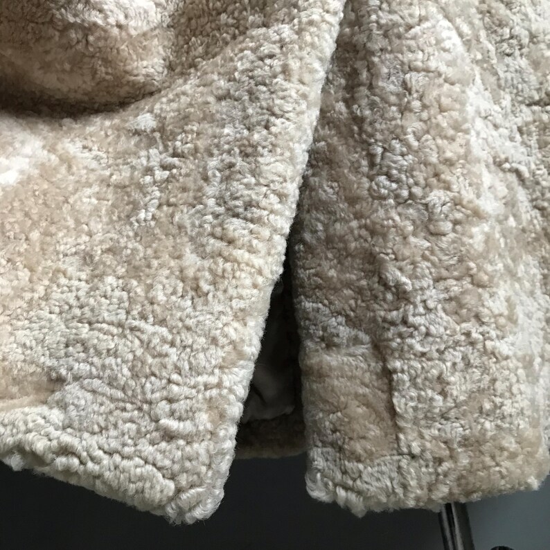 Op de afbeelding: Close-up van een beige nep bontstof met een zachte, pluche textuur. De stof is dubbelgevouwen, waardoor de binnen- en buitenkant van het materiaal zichtbaar is.