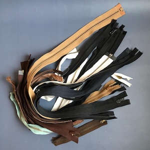 May include: A collection of different coloured zippers, including brown, black, white, and tan. The zippers are all in various lengths and have different types of pulls.