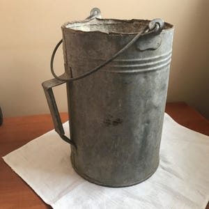 Puede incluir: Un cubo de metal galvanizado vintage con asa y un asa de alambre. El cubo está desgastado y muestra signos de uso.