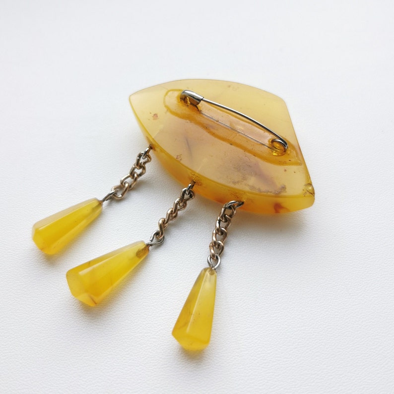 Op de afbeelding: Een vintage amber broche met een traanvorm en drie hangende amberdruppels bevestigd aan een zilveren ketting. De broche heeft een veiligheidsspeld sluiting.