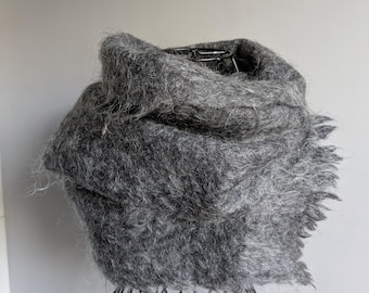 May include: A charcoal gray infinity scarf made of a fuzzy, textured knit material. The scarf features a thick, voluminous drape with a soft, brushed appearance and visible loose fibers throughout the fabric, creating a cozy and layered look.