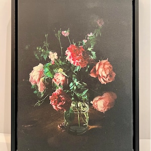 May include: A bouquet of pink and red roses in a clear glass vase on a dark wooden table. The roses are arranged in a loose, natural style, and the vase is simple and elegant.