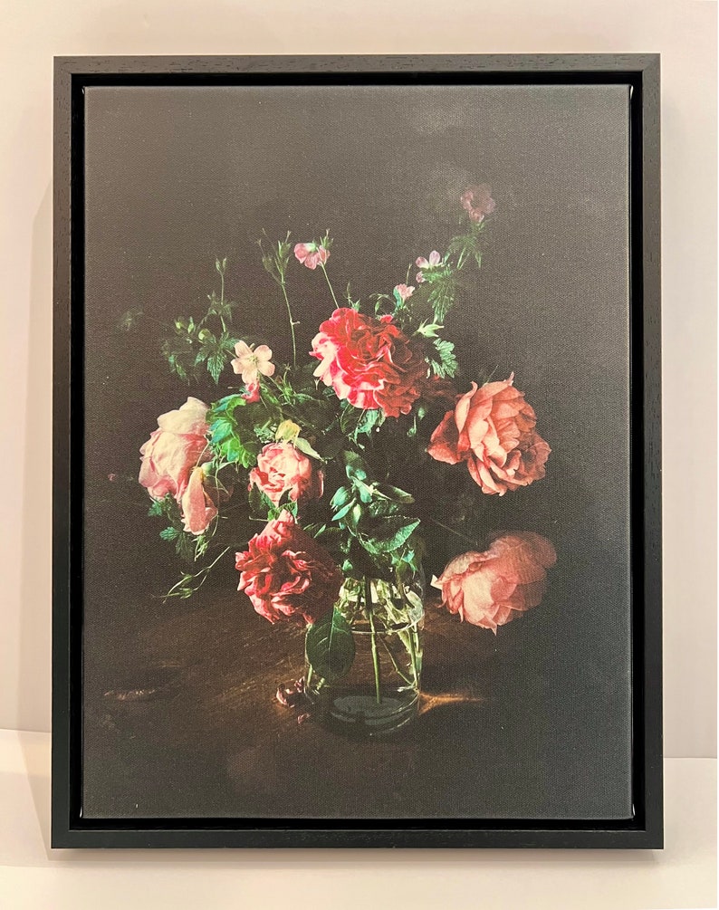 May include: A bouquet of pink and red roses in a clear glass vase on a dark wooden table. The roses are arranged in a loose, natural style, and the vase is simple and elegant.