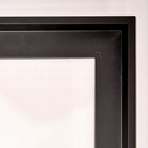 May include: Close-up of the top corner of a black picture frame. The frame has a double border.