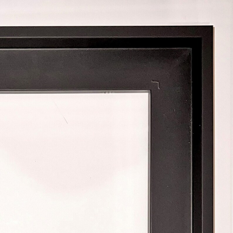 May include: Close-up of the top corner of a black picture frame. The frame has a double border.