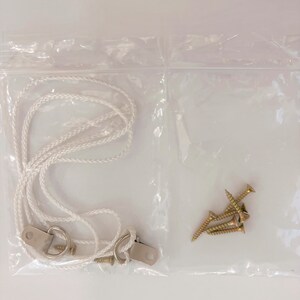 May include: A clear plastic bag containing a white rope, two metal hooks, and four gold screws.