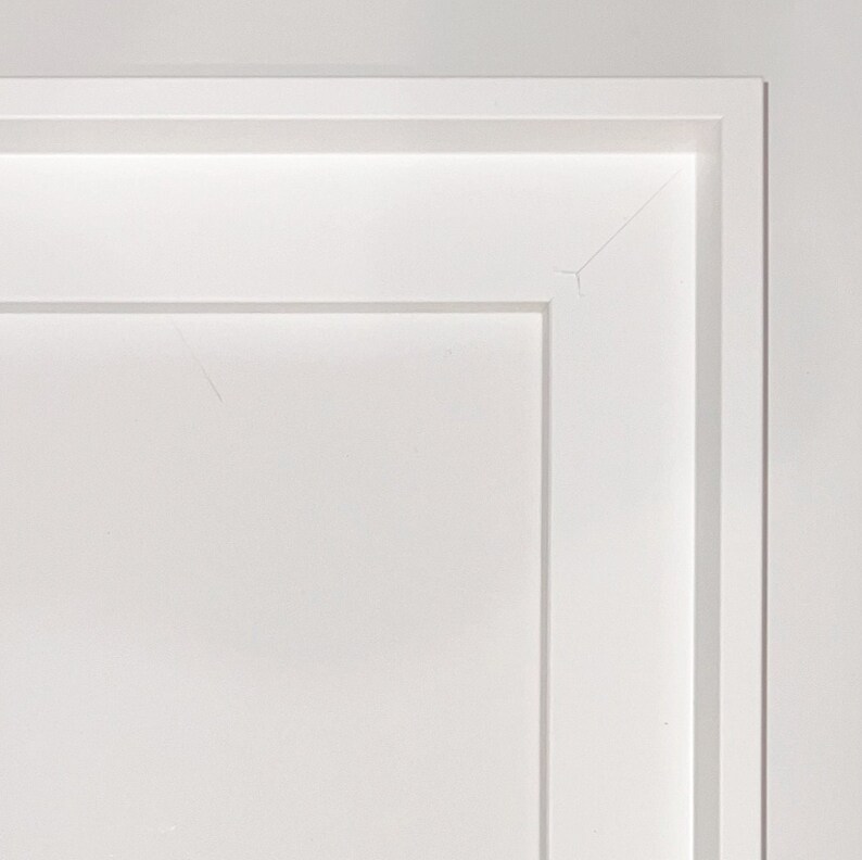 May include: A white picture frame with a simple, clean design. The frame has a slightly raised edge around the perimeter.