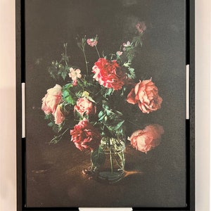 May include: A framed print of a still life featuring a bouquet of pink and red roses in a clear glass vase. The roses are arranged in a vase on a dark wooden table. The background is a dark, textured canvas.