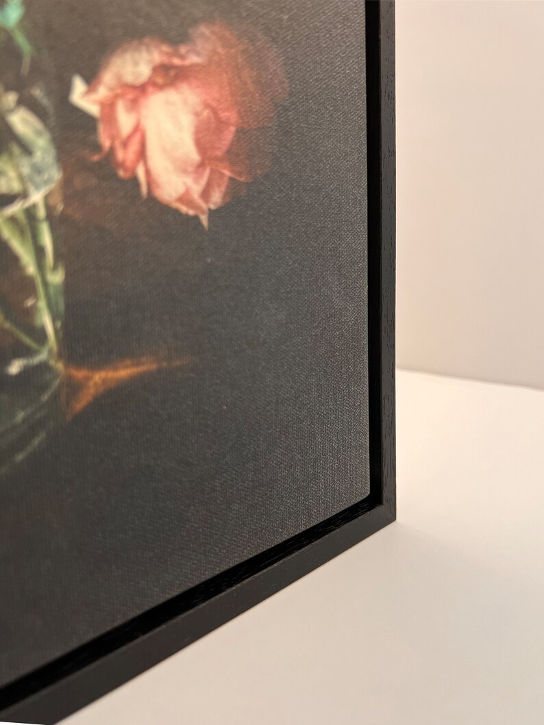 May include: A framed canvas print of a still life featuring a bouquet of pink and green flowers. The canvas is stretched over a black wood frame.