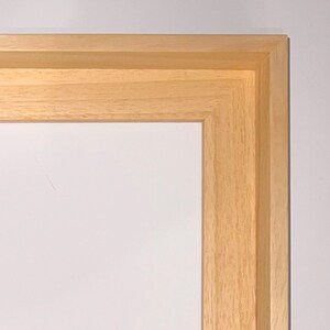 May include: Close-up of the corner of a natural wood picture frame. The frame is made of solid wood with a light brown finish.