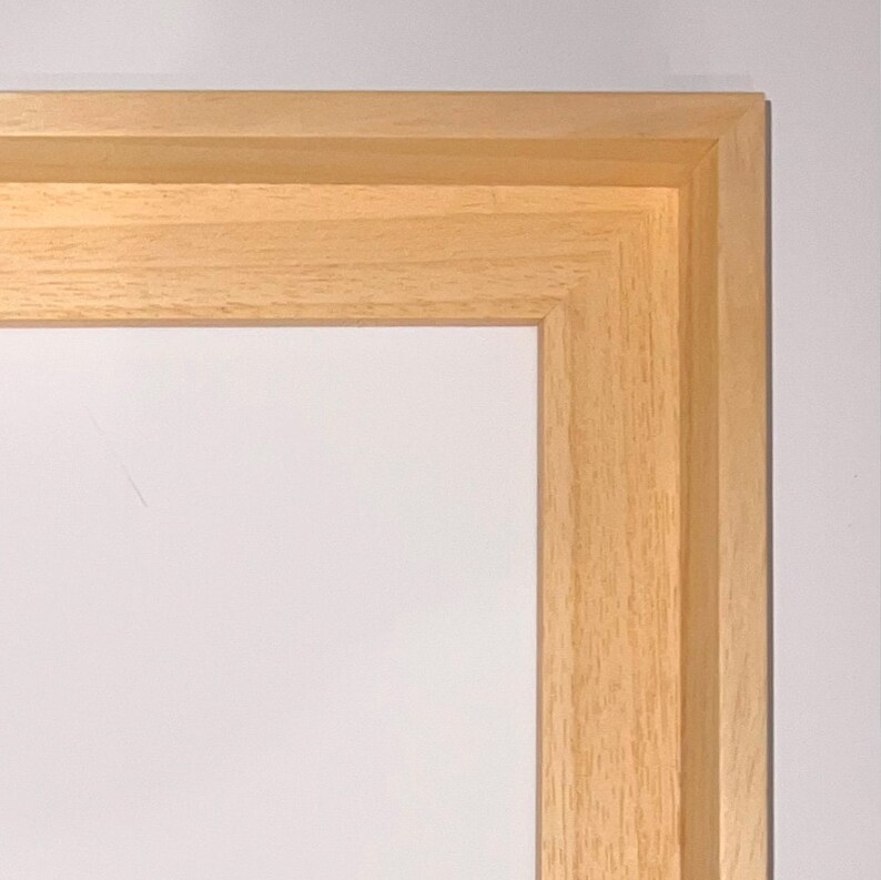 May include: Close-up of the corner of a natural wood picture frame. The frame is made of solid wood with a light brown finish.