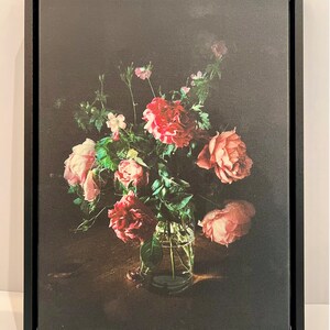 May include: A bouquet of pink and red roses in a clear glass vase on a dark wooden table. The roses are arranged in a loose, natural style, and the vase is simple and elegant.