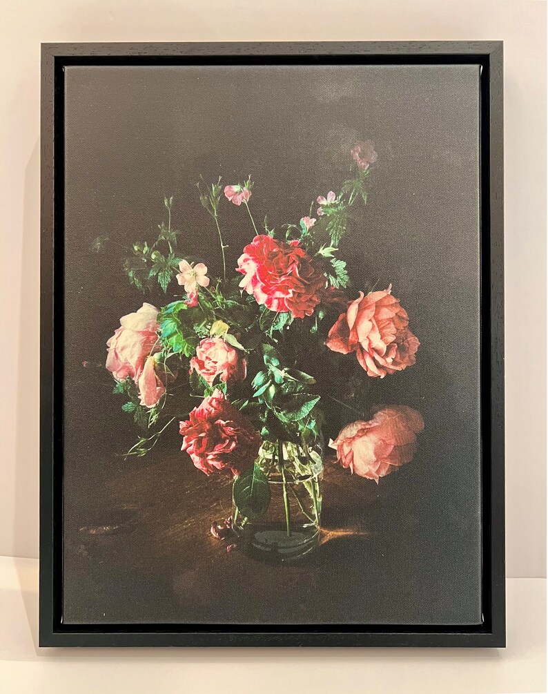 May include: A bouquet of pink and red roses in a clear glass vase on a dark wooden table. The roses are arranged in a loose, natural style, and the vase is simple and elegant.