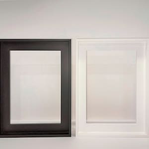 May include: Two picture frames, one black and one white, are displayed on a white surface. Both frames are rectangular and have a simple design.