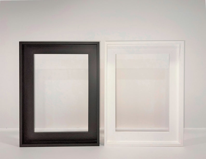 May include: Two picture frames, one black and one white, are displayed on a white surface. Both frames are rectangular and have a simple design.