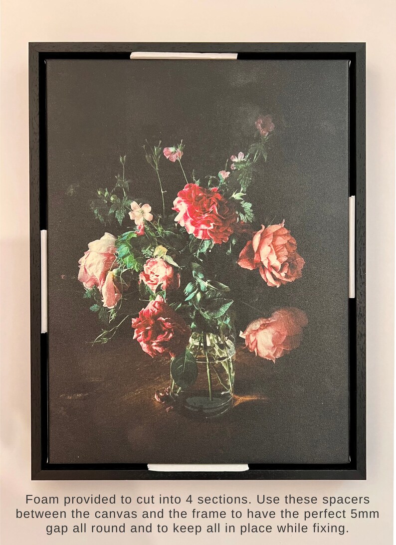 May include: A framed print of a still life featuring a bouquet of pink and red roses in a clear glass vase. The roses are arranged in a vase on a dark wooden table. The background is a dark, textured canvas.