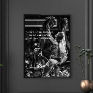May include: Black and white photo of a mixed martial arts fighter raising his arms in victory after a fight. The photo is framed and hanging on a wall. The text on the photo reads "THERE'S NO TALENT HERE, THIS IS HARD WORK. THIS IS AN OBSESSION."
