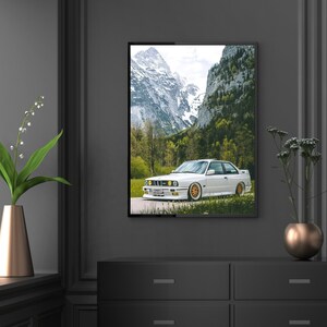 Puede incluir: Un coche deportivo BMW E30 M3 blanco aparcado frente a un paisaje de monta&ntilde;a. El coche tiene llantas doradas y est&aacute; de cara a la c&aacute;mara. El paisaje de monta&ntilde;a est&aacute; en el fondo y est&aacute; cubierto de nieve.
