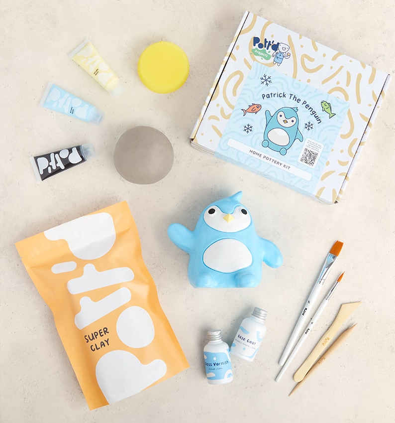K&ouml;nnte beinhalten: Ein Heim-T&ouml;pferset mit einer Pinguin-f&ouml;rmigen Form, blauer, wei&szlig;er und gelber Farbe, einem Beutel mit Ton und einer durchsichtigen Flasche Glasur. Das Set enth&auml;lt den Text "Patrick The Penguin" und "Home Pottery Kit".