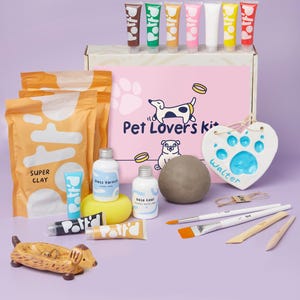 May include: A craft kit for making pet paw prints. The kit includes clay, paint, brushes, and a heart-shaped plaque. The plaque has the word "Walter" written on it. The kit is packaged in a pink box with the words "Pet Lovers Kit" on it.