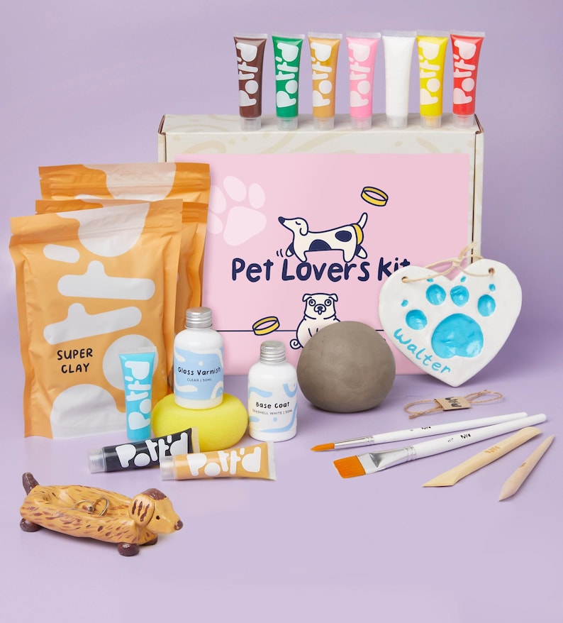May include: A craft kit for making pet paw prints. The kit includes clay, paint, brushes, and a heart-shaped plaque. The plaque has the word "Walter" written on it. The kit is packaged in a pink box with the words "Pet Lovers Kit" on it.
