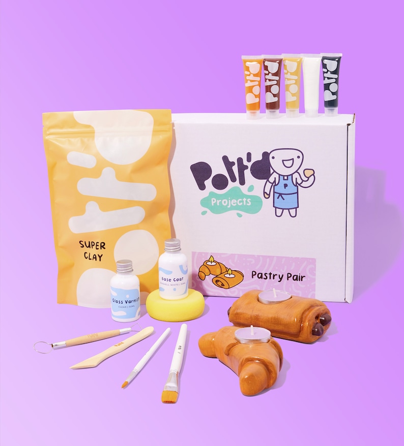 May include: A pottery craft kit with a white box that says "Pottery Projects" and "Pastry Pair". The kit includes a bag of clay, paint, brushes, and two unpainted croissant candle holders.